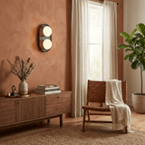 Sconce lit on a terracotta wall above a sideboard with a vase and books