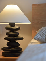 Unique table lamp in a dark finish lit beside a made bed