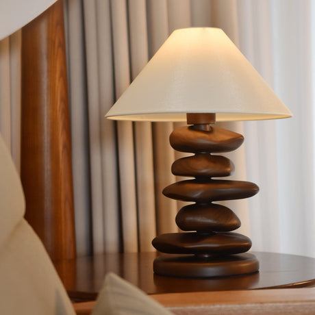 Close view of a dark wood pebble stack lit under the cream shade