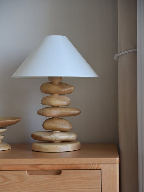 Unique table lamp in light wood on a dresser beside a wall
