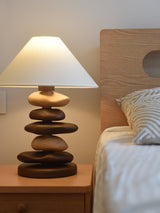 Unique table lamp with a mixed stack lit beside a woven headboard