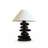 Unique table lamp with a matte black pebble stack on a plain ground