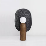 Table lamp with a charcoal carved backplate behind a lit opal glass globe