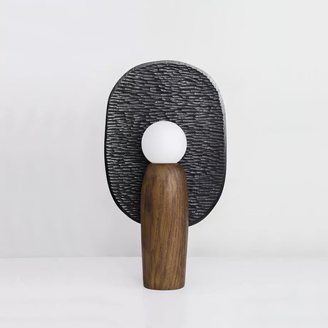 Table lamp with a charcoal carved backplate behind a lit opal glass globe