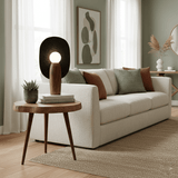 Totem table lamp lit on a round side table beside a cream sofa