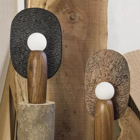 Two totem table lamps standing on cut wood stumps against a timber wall
