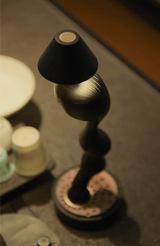Matte black cordless table lamp lit close up beside pale ceramics