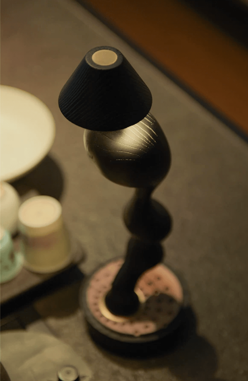 Matte black cordless table lamp lit close up beside pale ceramics