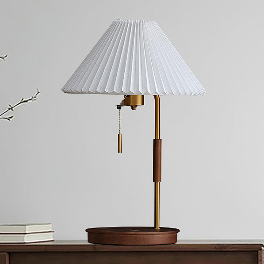 Table lamp with a beige pleated shade seen front on against a pale wall