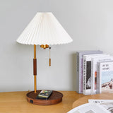 Table lamp lit on a desk with a phone flat on the base and books behind