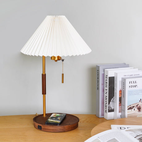 Table lamp lit on a desk with a phone flat on the base and books behind
