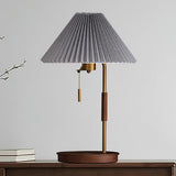 Table lamp with a gray pleated shade on a walnut base against a pale wall