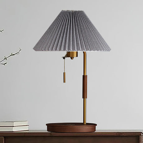 Table lamp with a gray pleated shade on a walnut base against a pale wall