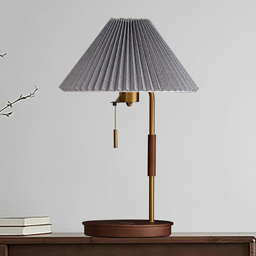 Table lamp with a gray pleated shade on a walnut base against a pale wall