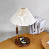 Table lamp lit on a desk with a phone charging flat on the walnut base