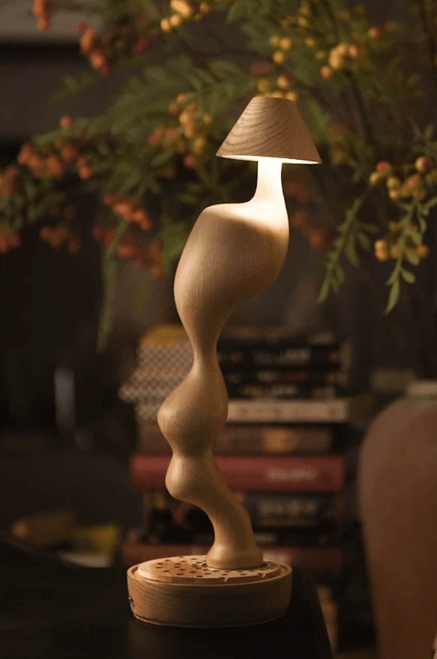 Cordless carved wood table lamp lit on a shelf among leaves and berries