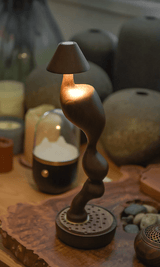 Cordless carved wood table lamp lit on a shelf beside pottery