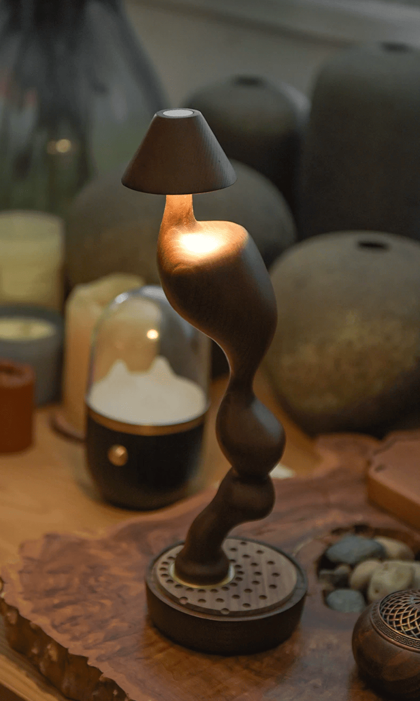 Cordless carved wood table lamp lit on a shelf beside pottery