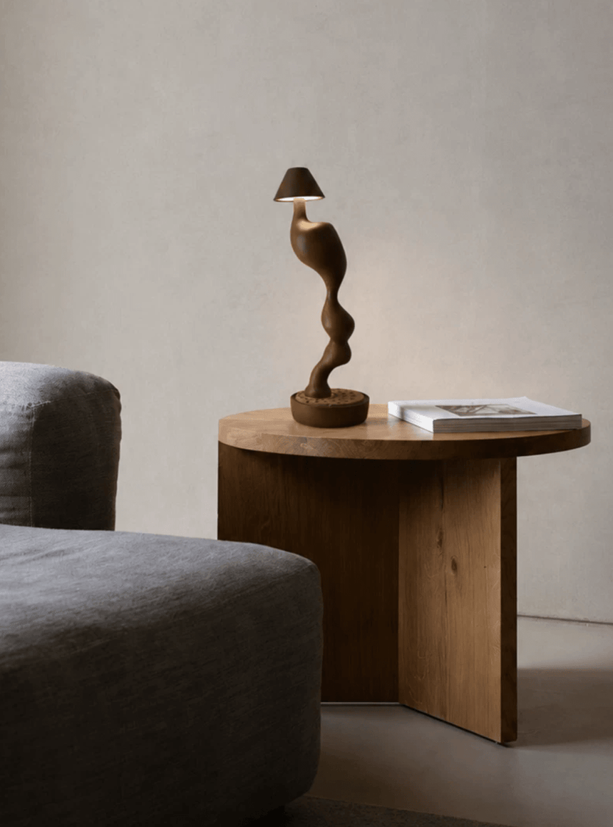 Cordless carved wood table lamp lit on a wooden side table by a chair