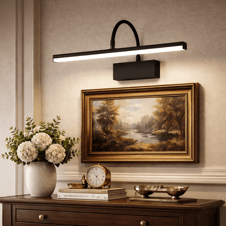 Black bar lit above a gilt framed landscape over a chest with flowers and a clock