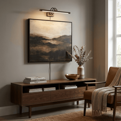 Dark bronze bar lit over a dark landscape canvas above a low walnut console and chair