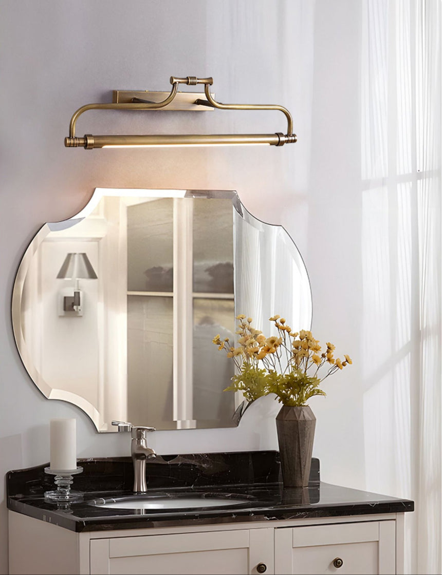 Warm metal bracket lit above a shaped mirror on a dark stone vanity by a window