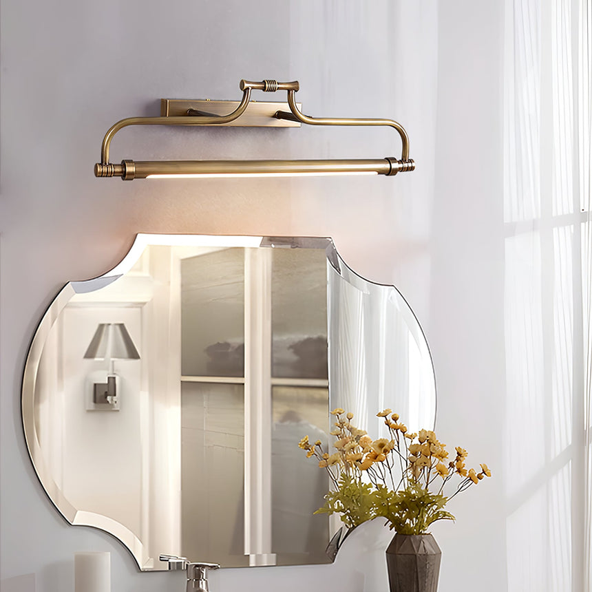 Warm metal bracket lit above a shaped mirror over a vanity with a vase of flowers