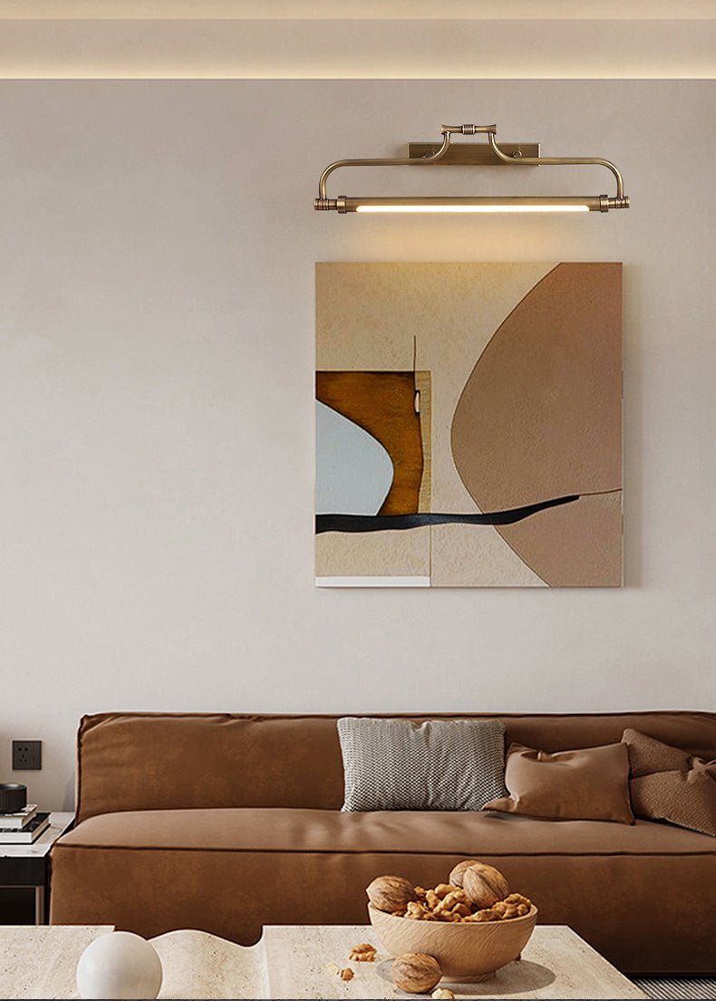 Bracket lit above a framed canvas on the wall behind a tan sofa and a low table
