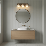 Three domes lit above a round mirror and a basin on a pale wood vanity