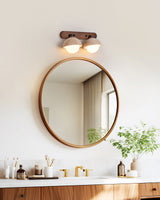 Two domes lit above a round mirror on a wood vanity with a plant beside