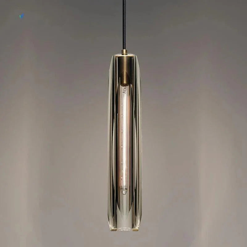 A slim copper and glass pendant lit against a dark painted wall