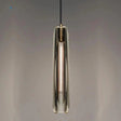 A slim copper and glass pendant lit against a dark painted wall