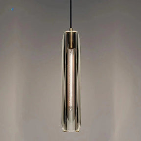 A slim copper and glass pendant lit against a dark painted wall
