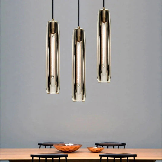 Three slim copper and glass pendants lit above a wooden sideboard
