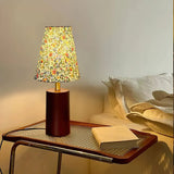 Floral shade lamp lit on a cane side table beside a bed