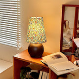 Floral shade lamp lit on a desk beside a window with blinds