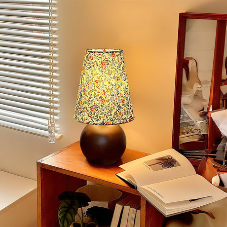 Floral shade lamp lit on a desk beside a window with blinds