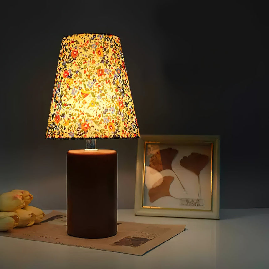 Floral shade lamp lit against a dark wall beside a framed print