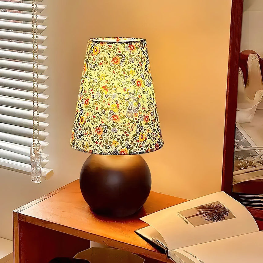 Floral shade lamp lit on a wood desk beside an open book