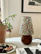 Floral shade lamp unlit on a shelf beside a small potted plant