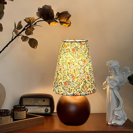 Floral shade lamp lit beside a small ceramic figure and a radio