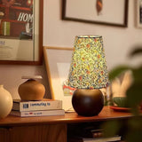 Floral shade lamp lit on a sideboard beside plants and a frame