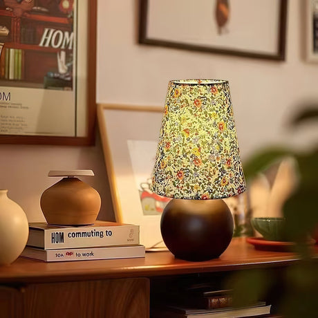 Floral shade lamp lit on a sideboard beside plants and a frame