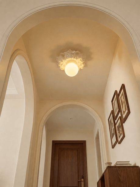 Carved floral ceiling light in a curved plaster corridor with a gallery wall