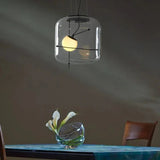 A glass drum pendant lit above a blue table with a glass object
