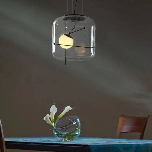 A glass drum pendant lit above a blue table with a glass object
