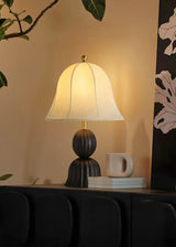 Black based vintage table lamp lit on a dark unit beside a white mug