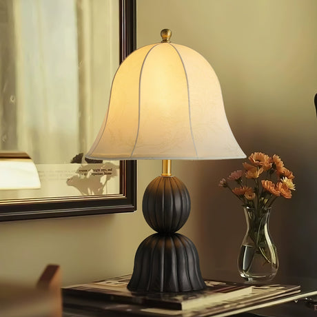 Black based vintage table lamp on a console beside a glass of flowers