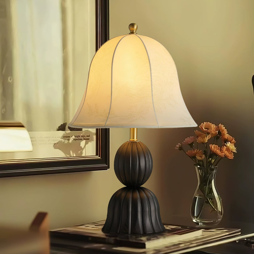 Black based vintage table lamp on a console beside a glass of flowers