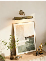 Scrolled brass bar lit over a framed canvas leaning above a console